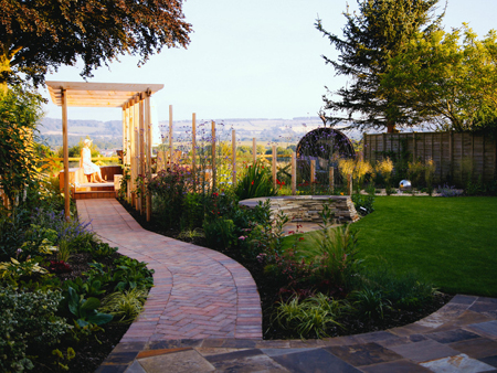 A curved path leads through a cedar pergola to a raised hardwood deck, where a woman sits in the glow of the afternoon sun, enjoying the view. Click image for more details.