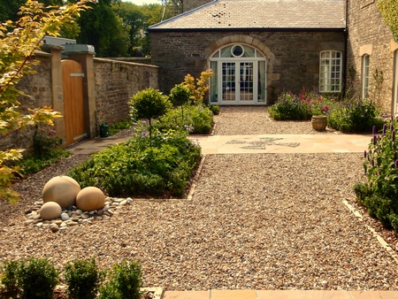 A large traditional stone courtyard garden designed with enclosing gravel paths, formal parterre beds and a stone sphere water feature. Click image for more details.