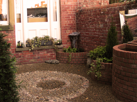 A decorative tiny brick courtyard garden with semi-circular raised beds and a raised pond backed by a mirror. Click image for more details.
